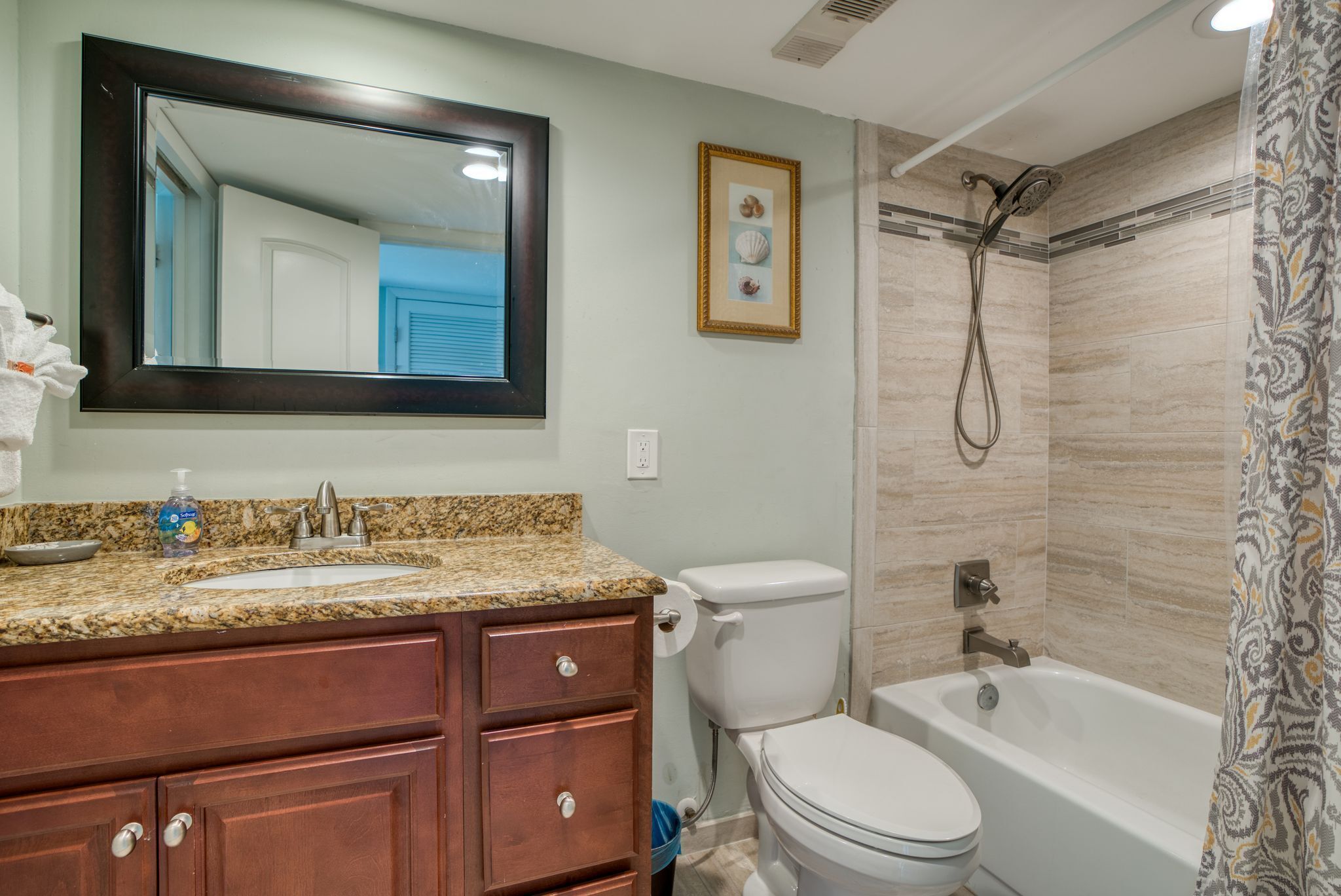 A bathroom with a granite countertop sink, a toilet, a bathtub, and a shower.