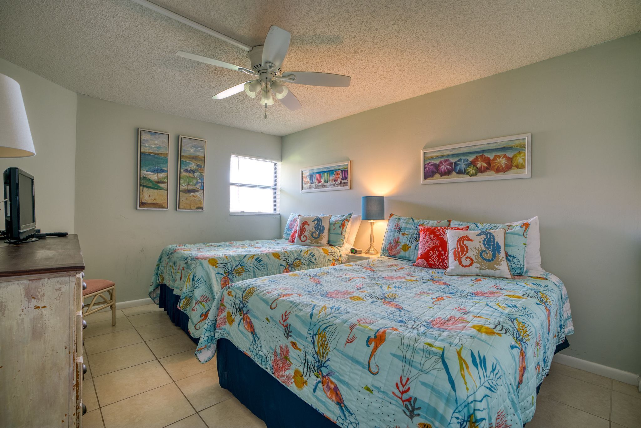 A bedroom with two beds, a ceiling fan, and artwork on the walls.
