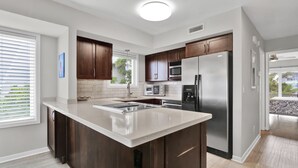 A modern kitchen with dark wood cabinets, stainless steel appliances, and a large island. - Oceanfront Townhome with Amazing Ocean Views (Wrightsville Beach)