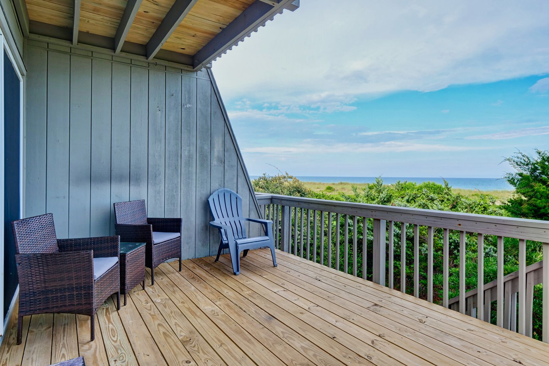 Une terrasse en bois, meublée de mobilier en osier, avec vue sur l’océan.