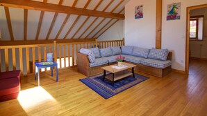 A cozy living room with a wooden ceiling, a checkered sofa, a small table, and a red chair.