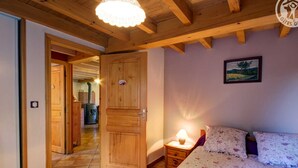 A bedroom with a wooden ceiling, a bed with floral bedding, a nightstand with a lamp, and a painting on the wall.