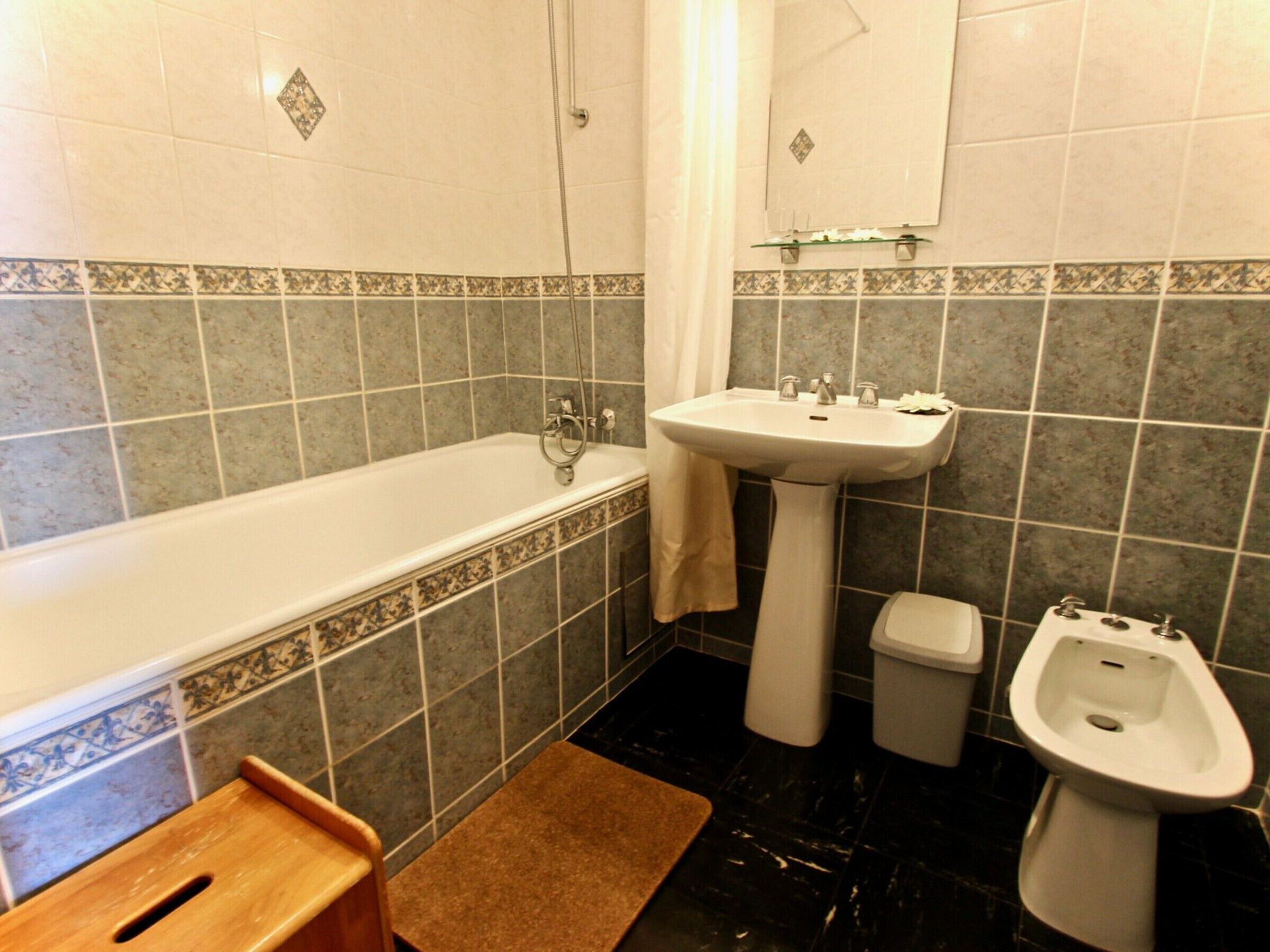 Un baño con bañera, lavabo, bidé y un taburete pequeño de madera.