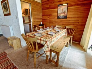 A dining area with a wooden table set for four, surrounded by wooden chairs. A plaque on the wall indicates the location as 'Hosotte'.