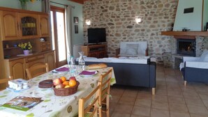 A cozy room with a stone wall, wooden ceiling beams, a television, a fireplace, and a dining area with a table set for two. - Cozy rental with garden, fireplace, and pet-friendly near Roanne (La Tuilière)