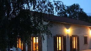 A two-story house with a tiled roof, wooden shutters, and a well-lit entrance. - Cozy rental with garden, fireplace, and pet-friendly near Roanne (La Tuilière)