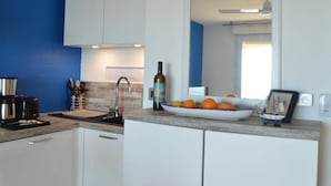 A modern kitchen with white cabinets, a blue accent wall, a stainless steel coffee maker, a wine bottle, and a fruit bowl.