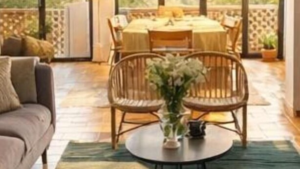 Un vaste espace de vie comprenant un canapé, une table basse ronde et des fauteuils en osier.