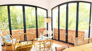 Une pièce baignée de lumière naturelle, dotée d'un mur en verre incurvé, de meubles en osier et d'une table ronde.