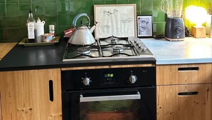 Une cuisine avec des carreaux verts, une cuisinière à gaz, un four, une bouilloire, un mixeur et une autre bouilloire posée sur un plateau.
