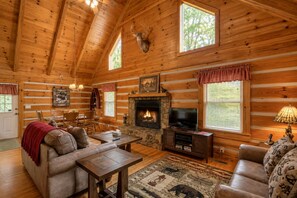 A log cabin interior with a fireplace, television, leather furniture, and a mounted deer head. - Cozy Cabin, Pet Friendly, Close to Town, Great Mountain Getaway for Relaxation (Morganton)
