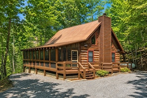 Une cabane en bois avec un toit en pente, une véranda à l’avant et une allée gravillonnée.