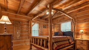 A log cabin bedroom with a four-poster bed, wooden walls, and a window with blinds.