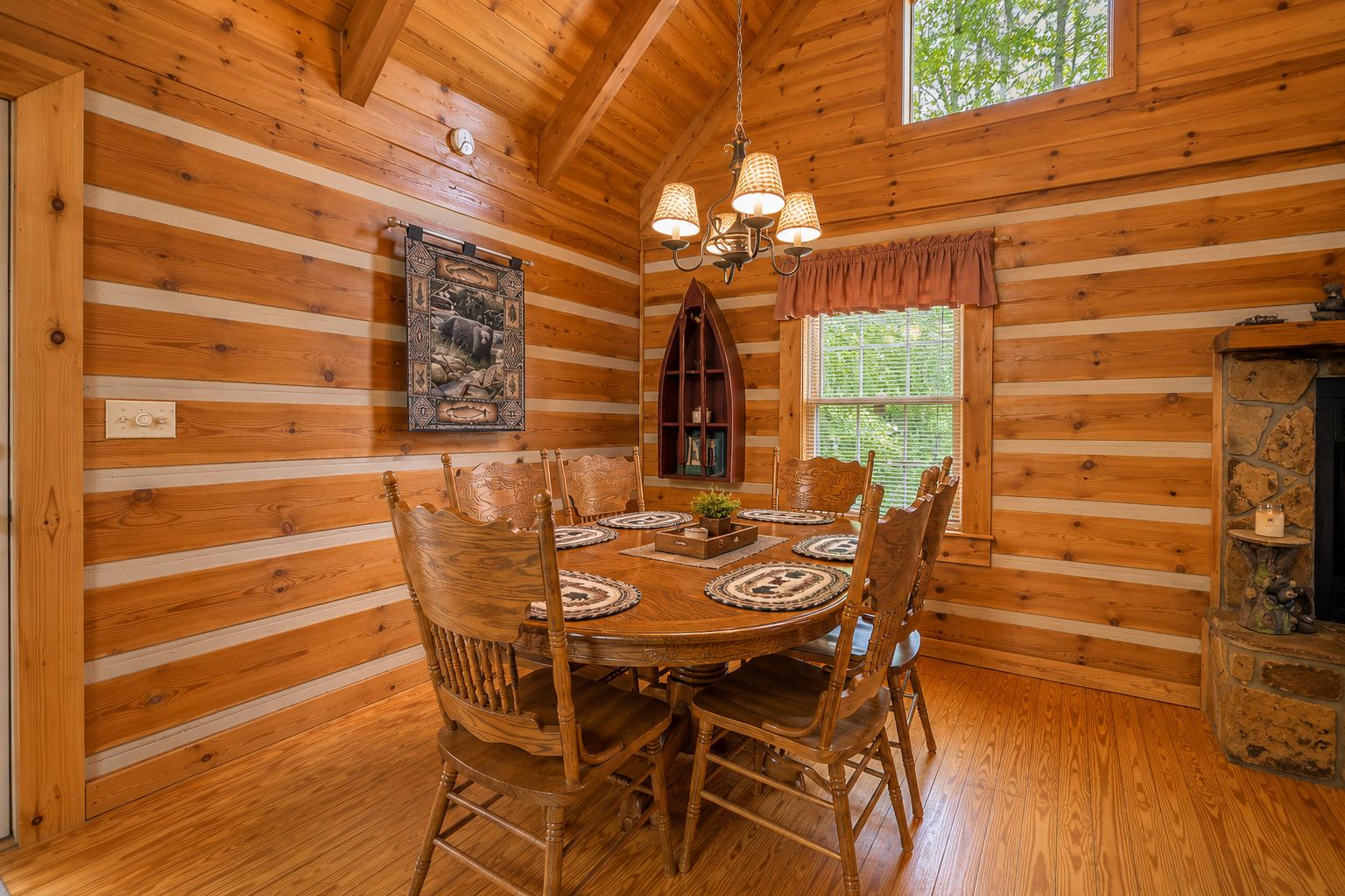 A wooden interior with a dining table, chairs, a chandelier, and a fireplace.