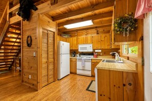 Une cuisine rustique aménagée dans une cabane en bois, comprenant un réfrigérateur, une cuisinière, un four à micro-ondes et des placards en bois.