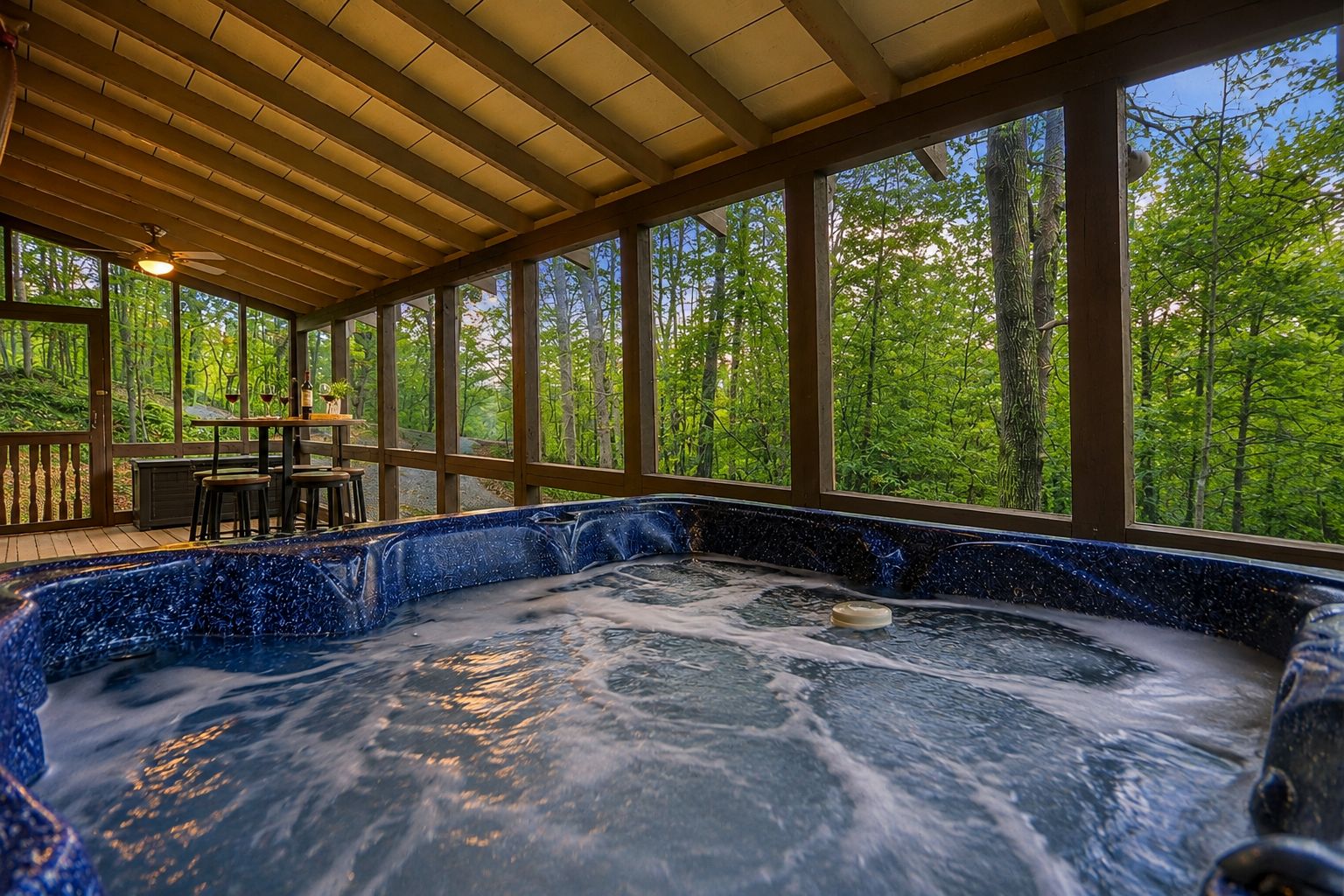 A hot tub with a view of a forest through large windows.