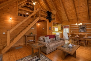 L’intérieur d’un chalet en bois, avec un escalier, un canapé, une table à manger et des chaises.