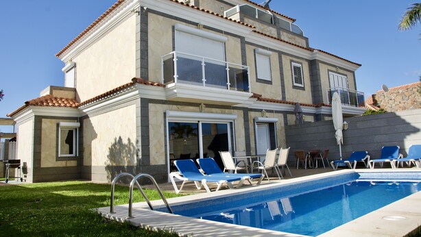 Une maison à deux étages avec une piscine, un espace salon extérieur et un mur en pierre.