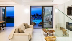 Una sala de estar moderna con sofá, mesa de centro y televisor. Hay una puerta de vidrio que da a un balcón con piscina.