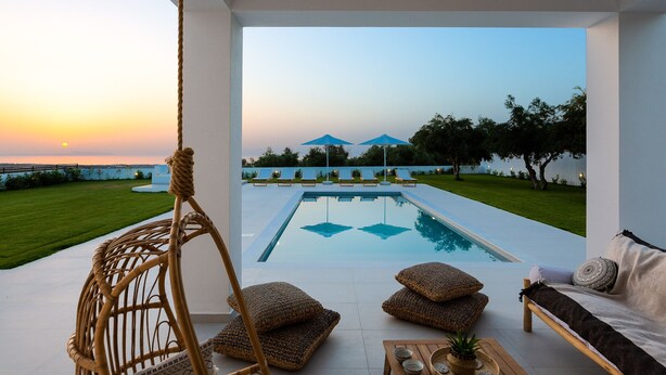Un área de piscina moderna al aire libre con vistas despejadas al atardecer, una silla de descanso, un sofá y una mecedora colgante.