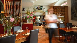Un restaurante con mesas y sillas de madera, una zona de bar y un cuadro grande en la pared.