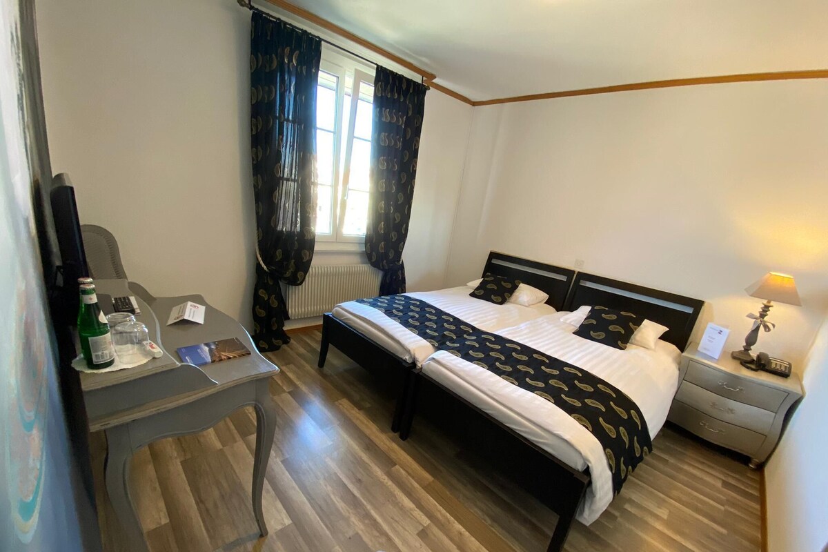 A hotel room with a bed, a desk, a chair, a nightstand, and a lamp.