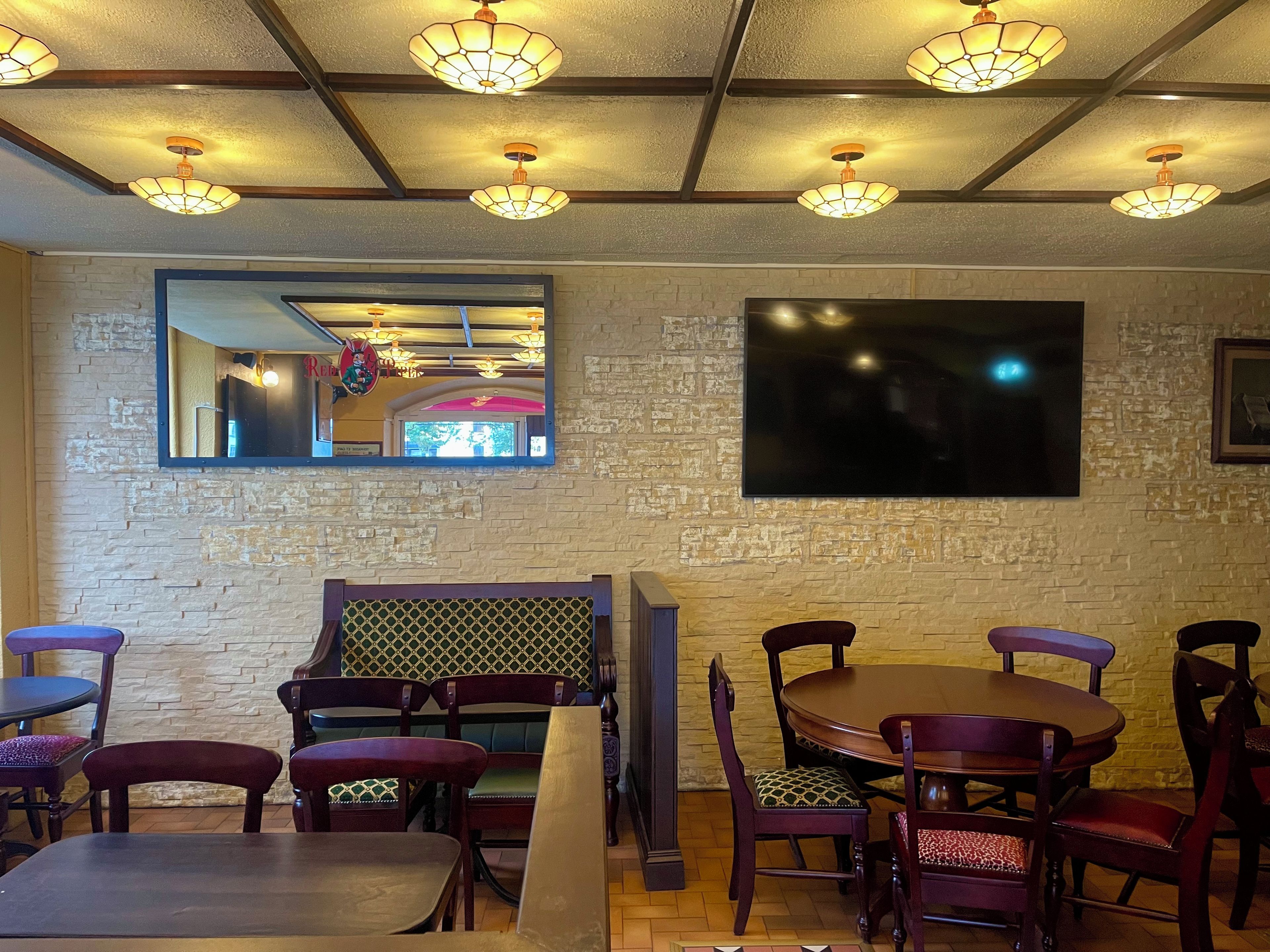 A restaurant interior with brick walls, wooden furniture, and a large flat-screen TV mounted on the wall.