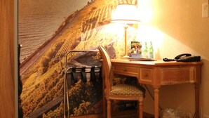 Una habitación con un escritorio de madera, una silla, una lámpara y un estante en la pared.