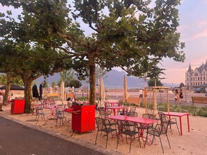 Outdoor seating with tables and chairs, a red cabinet, and a view of a building in the background. - Hostellerie de Genève (Vevey)