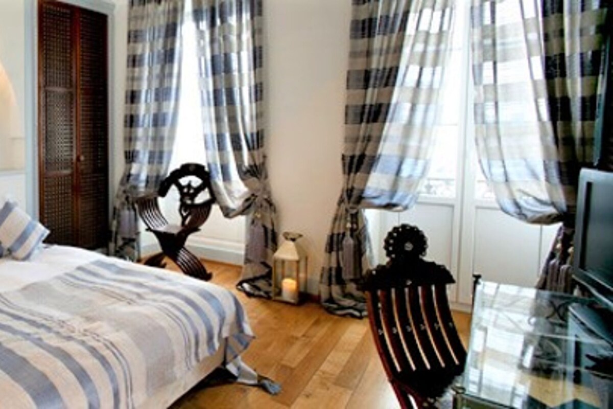 A bedroom with a bed, a chair, a TV, and a window with curtains.