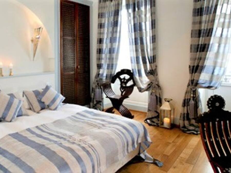 A bedroom with a bed, a chair, a TV, and a window with curtains.