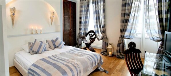 A bedroom with a bed, a chair, a TV, and a window with curtains. - Hostellerie de Genève (Vevey)