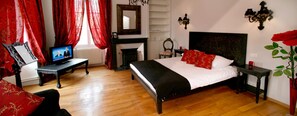 A bedroom with a bed, a television, a fireplace, and a red rose in a vase.