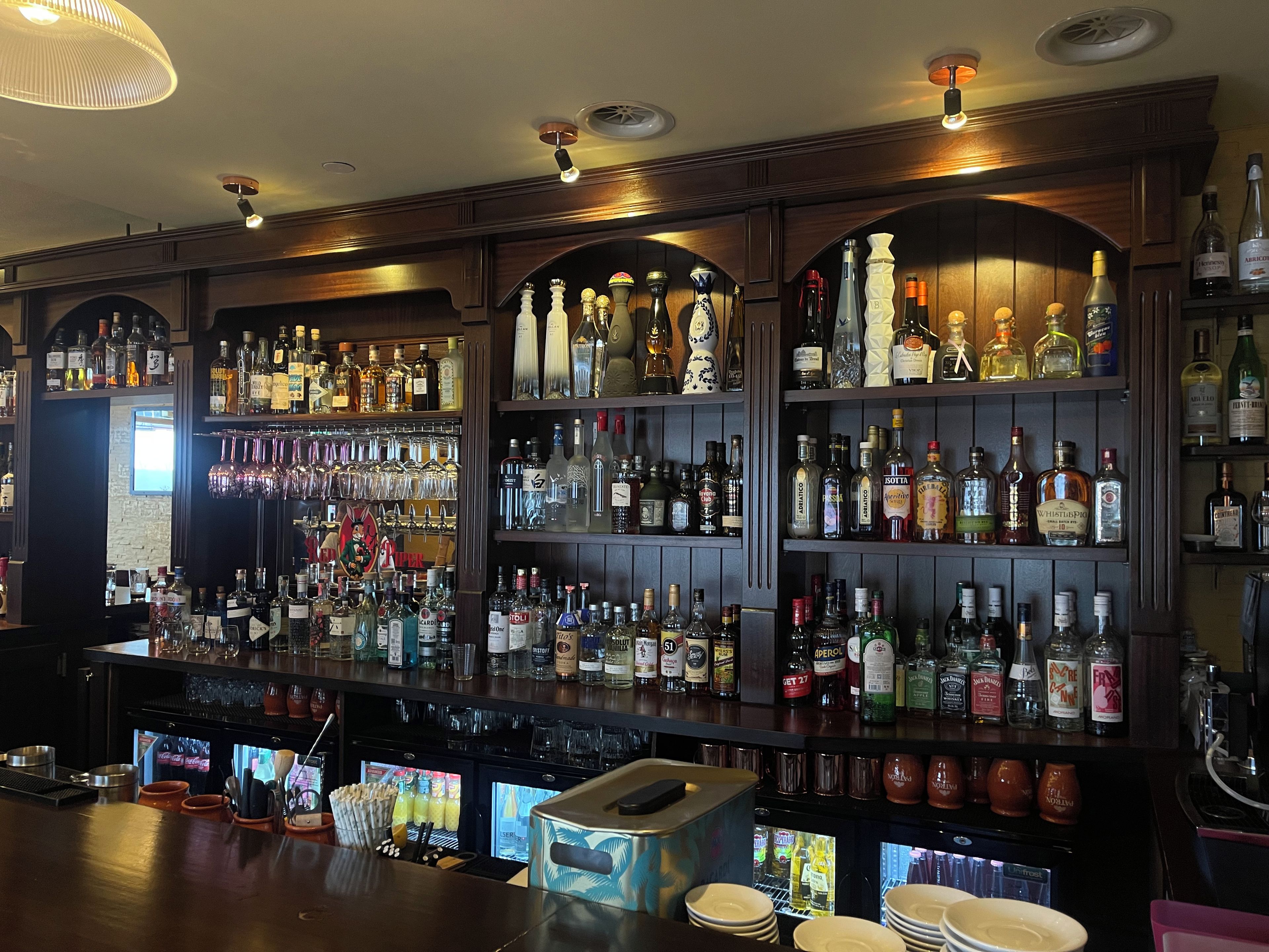 Un bar dont les étagères sont remplies de différentes bouteilles d’alcool et de verres.
