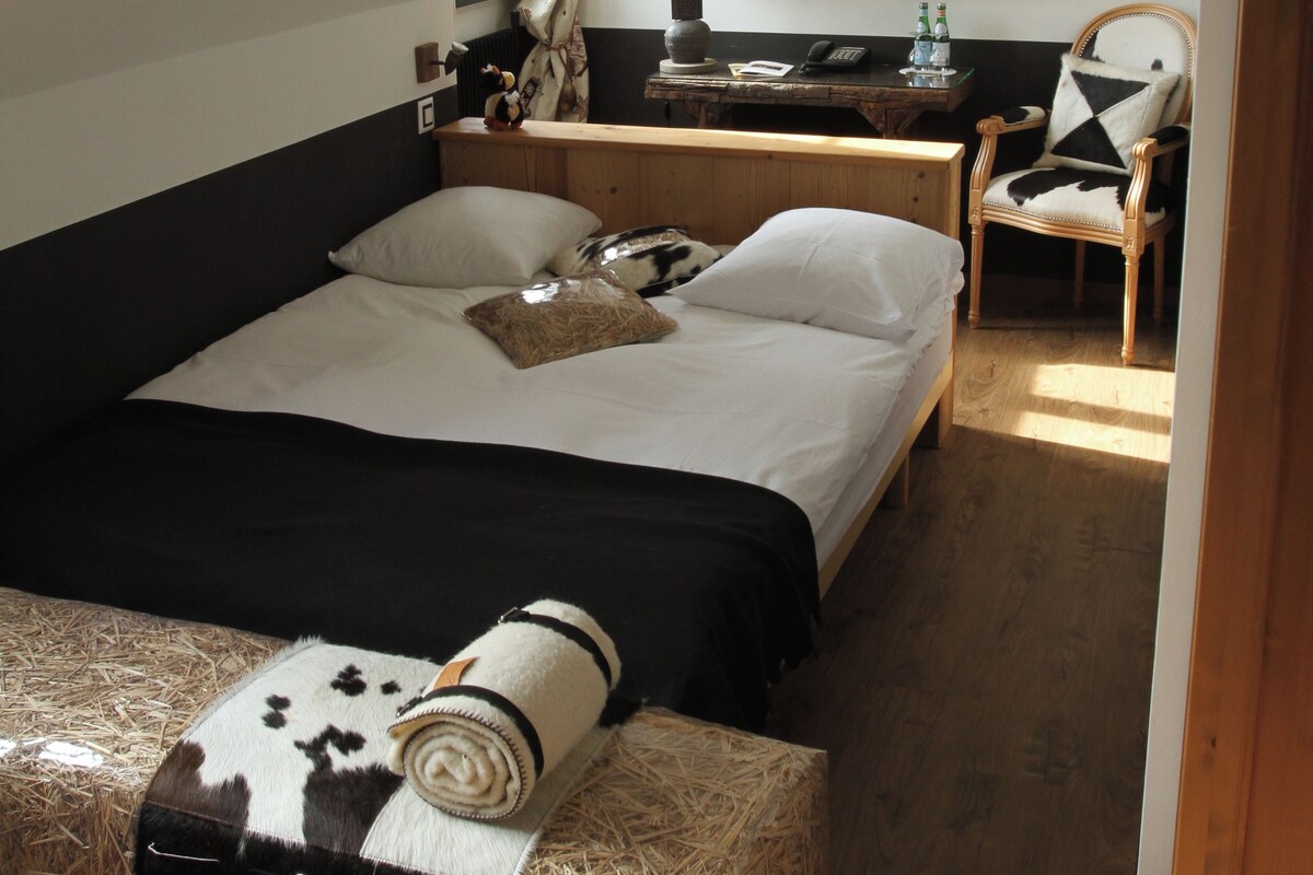 A bedroom with a bed, a wooden nightstand, a chair, and a desk with a lamp.