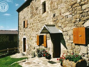 A stone building with a wooden door and windows, surrounded by a stone pathway and potted plants.