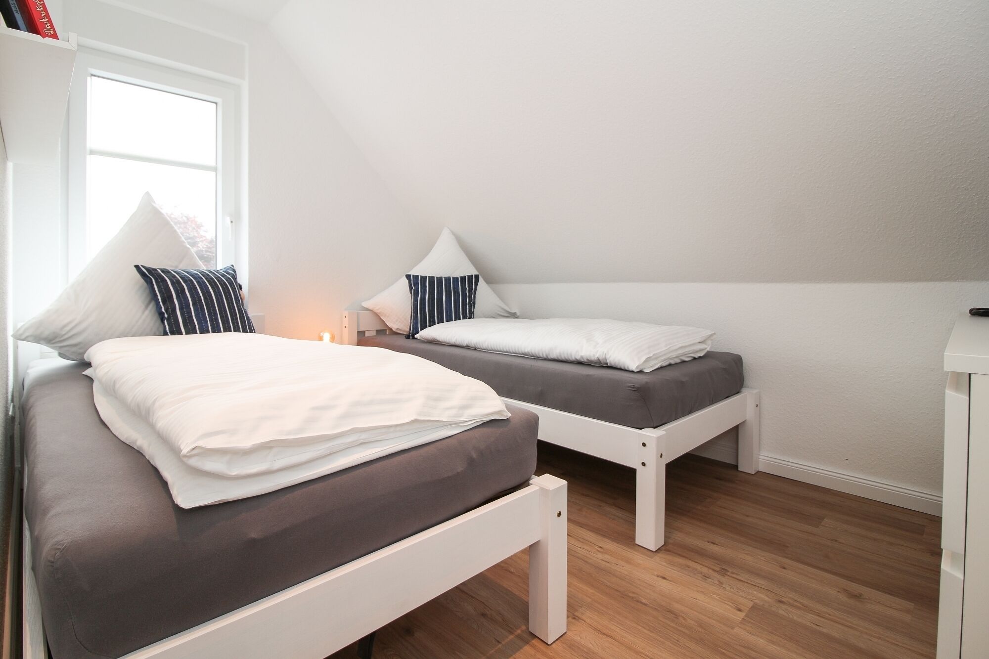 A bedroom with two beds, a window, and a bedside table with a lamp.