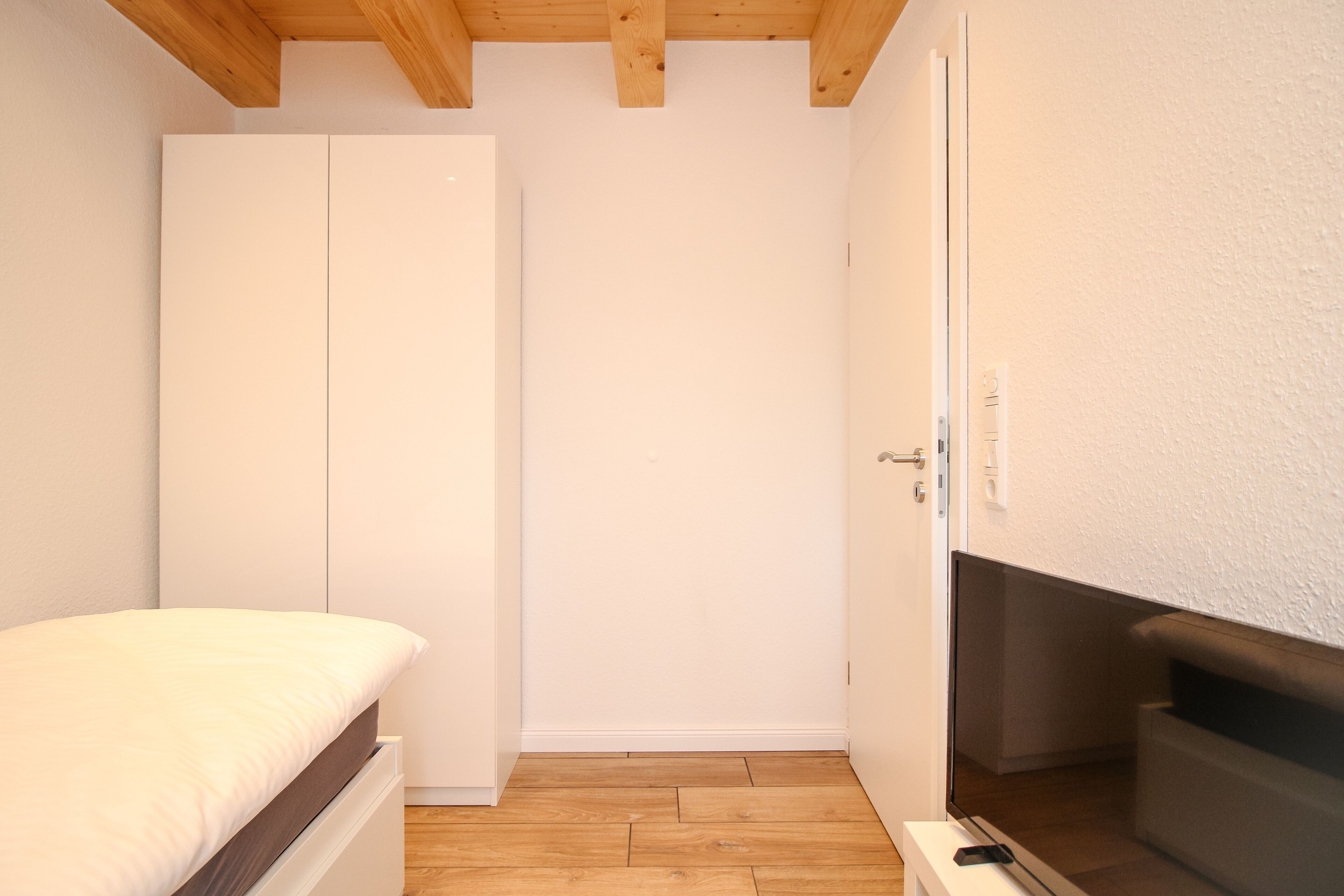 Een slaapkamer met een bed, een kledingkast, een televisie en een houten vloer.