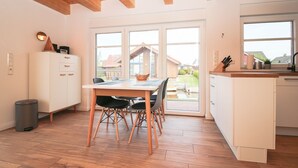 Une cuisine moderne avec un plancher en bois, une table à manger avec des chaises, un meuble blanc et une grande fenêtre donnant sur l’extérieur.