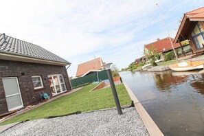 A residential area with a canal, houses with red roofs, and a grassy lawn. - High quality & detached holiday home for up to 4 persons + baby (NEW BUILDING!) (Südbrookmerland)