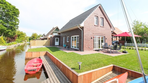 Une maison avec un quai, une pelouse et un bateau rouge.