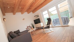 Un salon avec un plafond en bois, un canapé, un fauteuil, un téléviseur et une fenêtre donnant sur l’extérieur.
