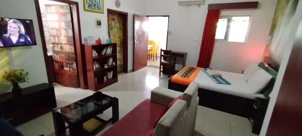 A living room with a sofa, a coffee table, a TV, a bookshelf, and a dining area with chairs. - PLEASANT STUDIO (Cocody)