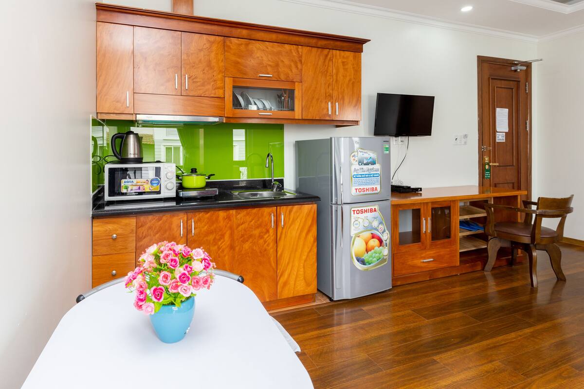 A compact kitchen with wooden cabinets, a microwave, a refrigerator, and a dining area with a table and chairs.