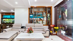 A modern living room with a sectional sofa, a coffee table, and a glass display cabinet with decorative items. - Sunny Hotel and Apartment (Ho Chi Minh City)
