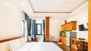 A hotel room with a large bed, a desk with a refrigerator, a TV, and a view of the city through the window. - Sunny Hotel and Apartment (Ho Chi Minh City)