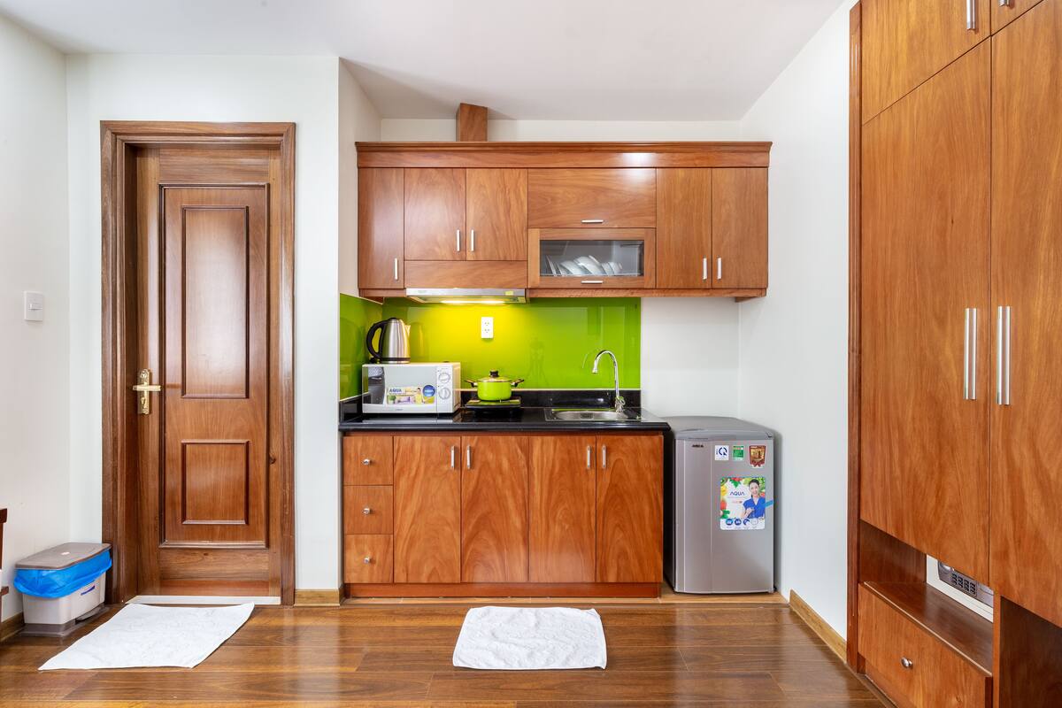 A compact kitchen with wooden cabinets, a microwave, a kettle, and a refrigerator.
