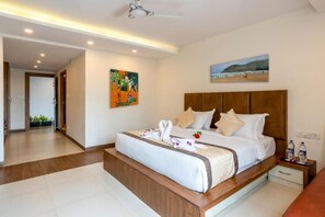 A modern hotel room with a large bed, a wooden headboard, a painting, and a view of the beach. - Amor Beach Resort (Candolim)
