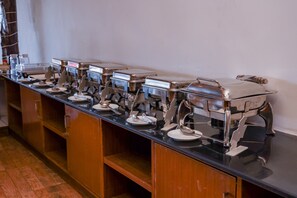 A buffet setup with multiple self-service stations, each equipped with a food container, plate, and serving utensils. - Amor Beach Resort (Candolim)