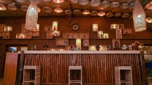 Un espace bar doté d’un comptoir en bois, de tabourets en osier et de luminaires suspendus.